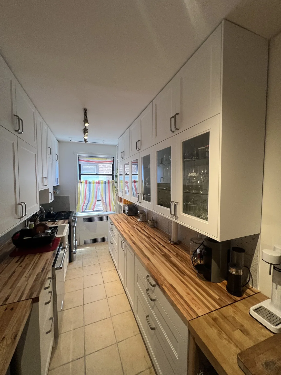 Finished white galley IKEA kitchen with butcher block countertops and glass-front cabinets